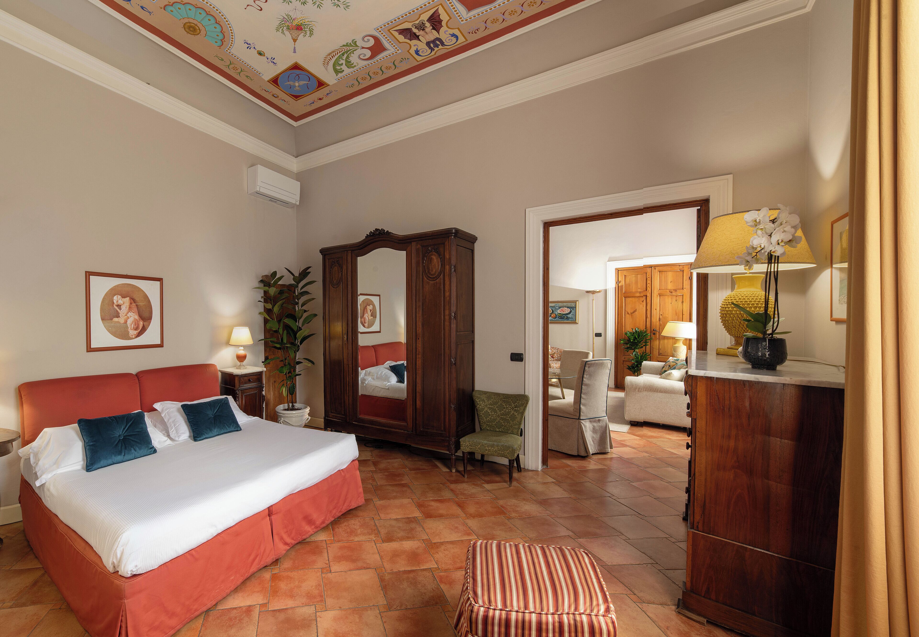 Un dormitorio con una cama grande, un armario, una silla y un escritorio con una lámpara.