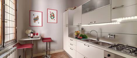A modern kitchen with white cabinets, a gas stove, a sink, and two red bar stools.