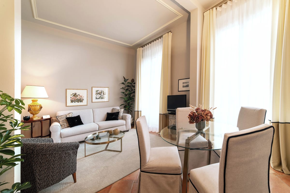 A modern living room with a sofa, two armchairs, a glass coffee table, and a TV.
