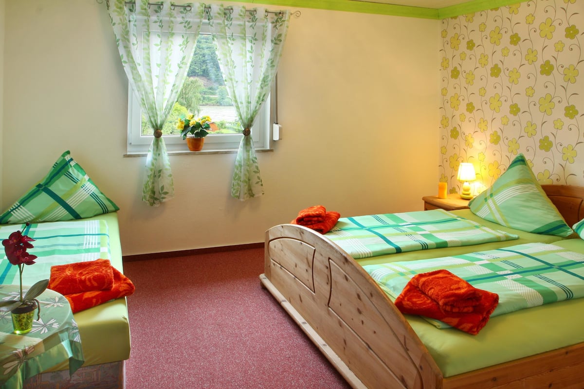 A bedroom with a bed, two bedside tables, a window with curtains, a potted plant, and a lamp.