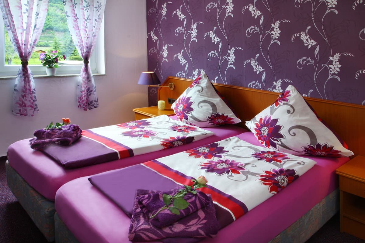 A double bed with floral bedding, a bedside table with a lamp, and a window with curtains.