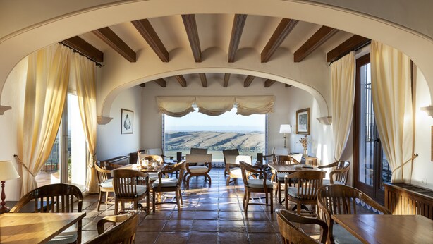 A dining area with a view of rolling hills, wooden furniture, and a vaulted ceiling.
