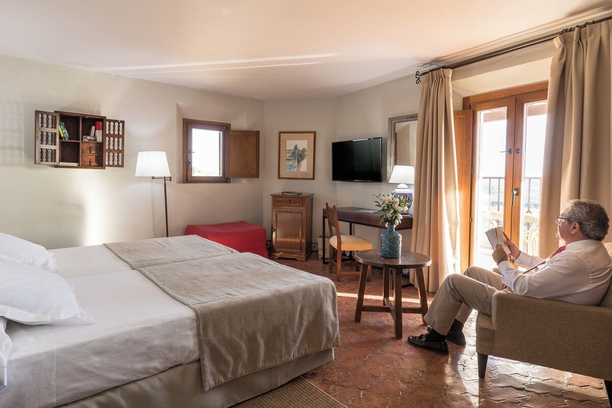 A hotel room with a bed, a desk, a chair, a TV, and a window with curtains.