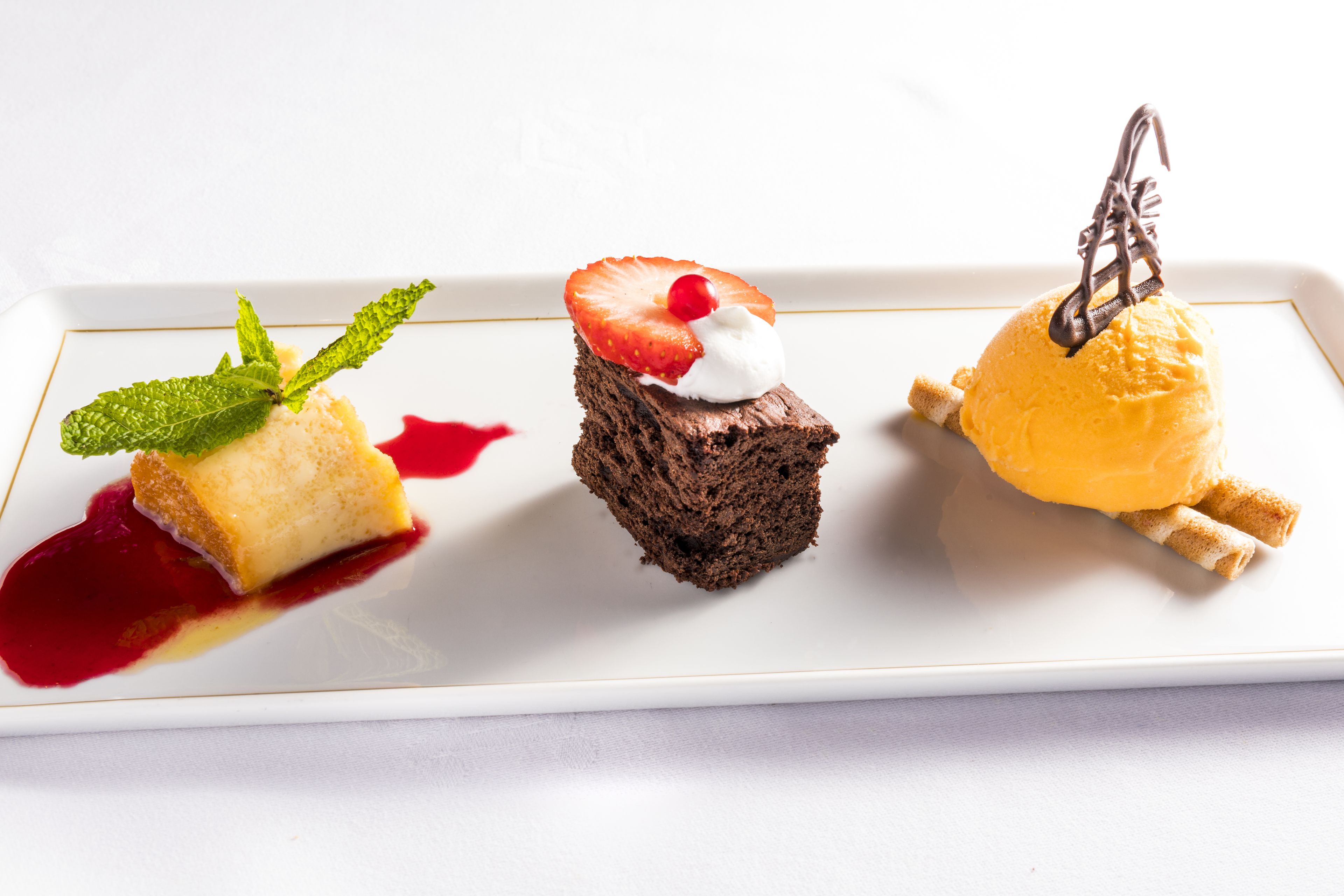 Trois desserts présentés sur une assiette blanche ornée d’un bord doré.