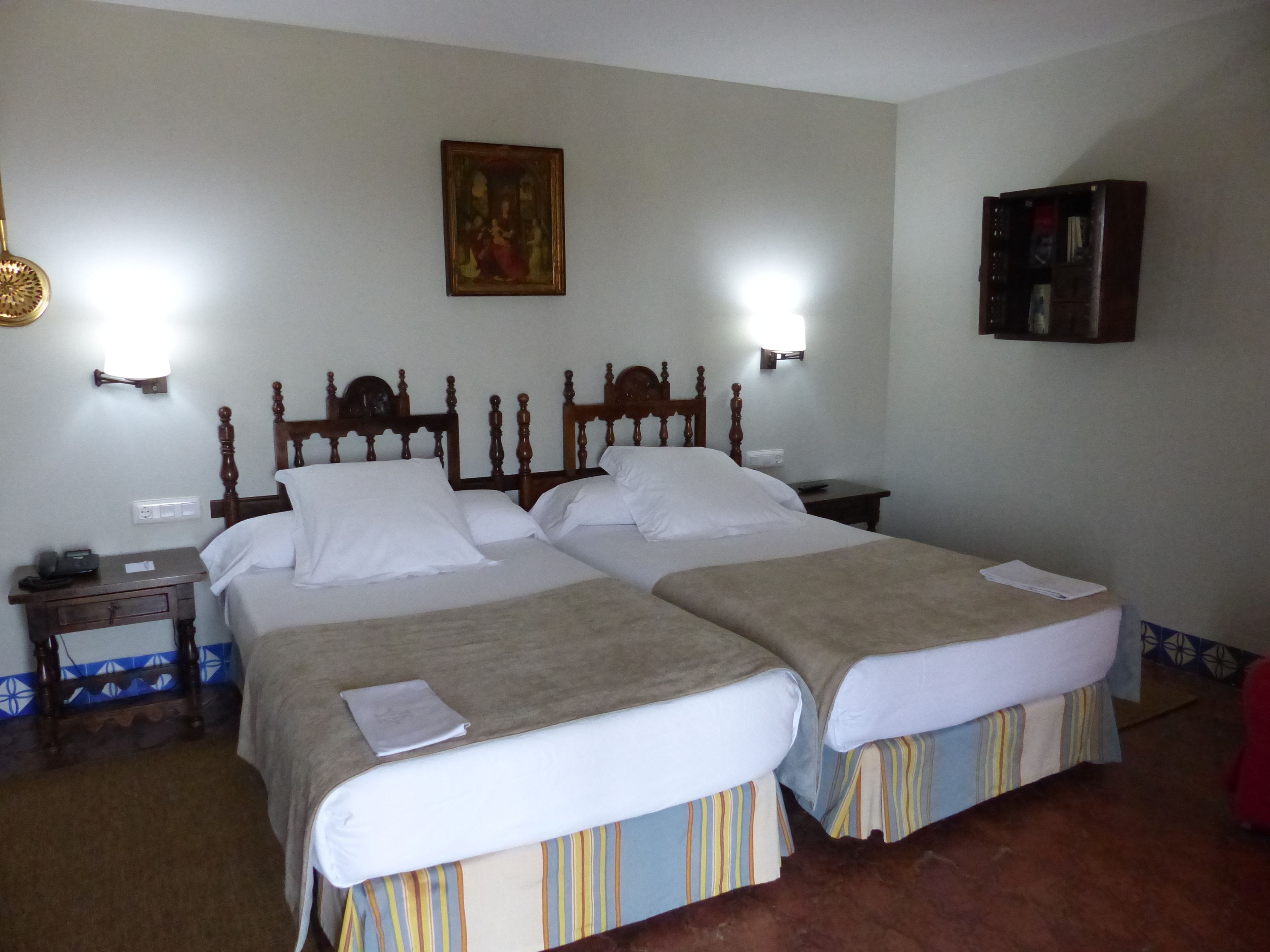 A hotel room with two beds, a nightstand, a lamp, a wall-mounted picture, and a cabinet.