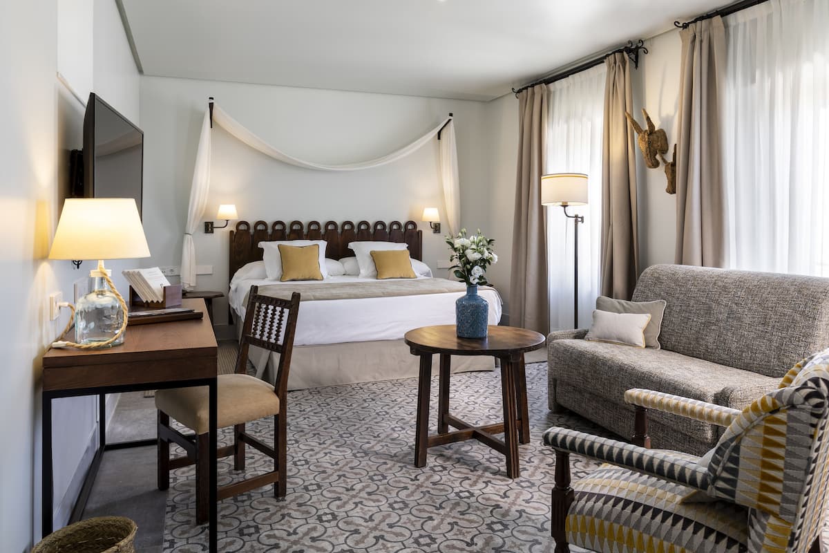 A hotel room with a bed, a desk, a chair, a sofa, and a small table.