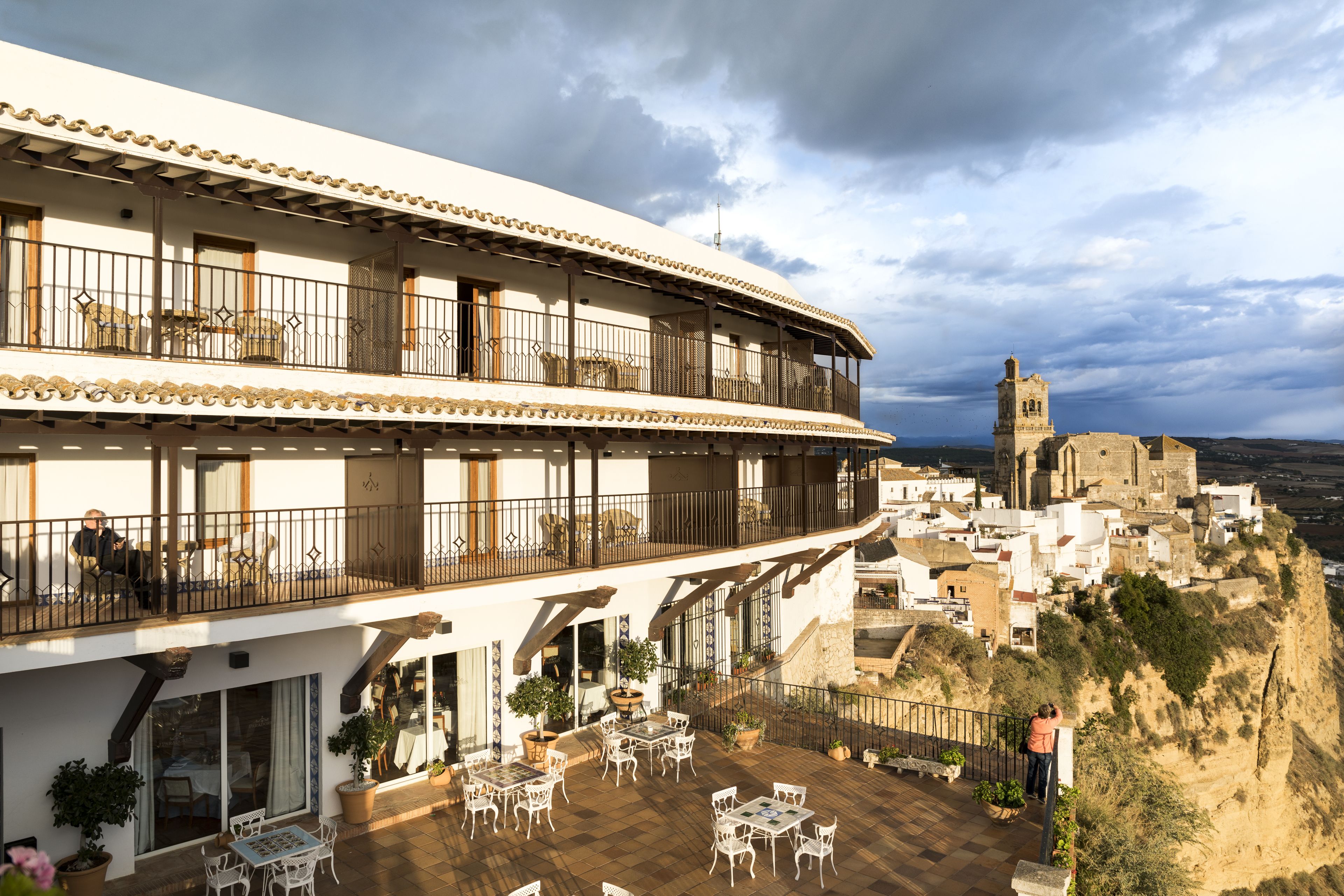 Un hotel con terraza que ofrece asientos al aire libre, vistas a un pueblo histórico y una imponente torre de iglesia al fondo.