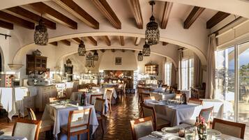 A restaurant with high wooden ceilings, arched windows, and hanging lanterns. Tables are set with white tablecloths and chairs.