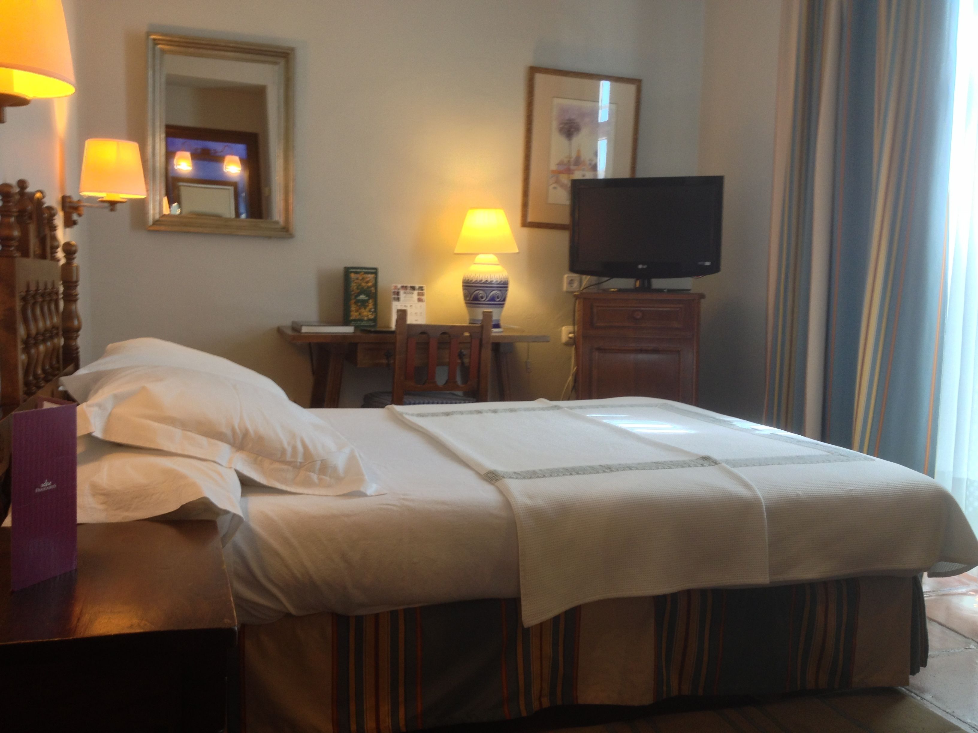 Une chambre d’hôtel équipée d’un lit, d’un bureau, d’une chaise, d’une télévision et d’une fenêtre avec des rideaux.