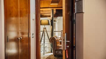 Una puerta de madera que da a una habitación con un sofá de cuero, un trípode y una lámpara.
