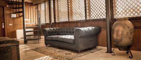 Una sala de estar con un sofá gris, un tapiz estampado, un jarrón grande y una escalera de madera.