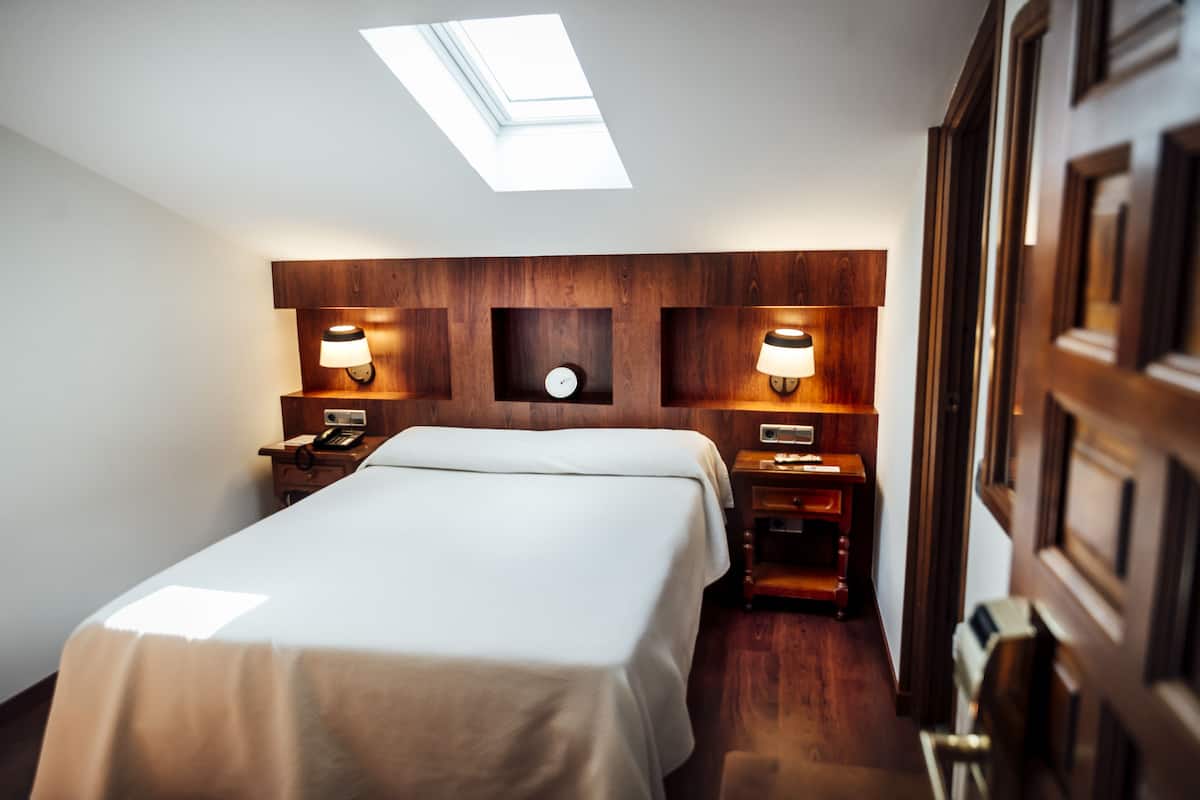 A hotel room with a skylight, a large bed, two bedside tables with lamps, and a wooden headboard.