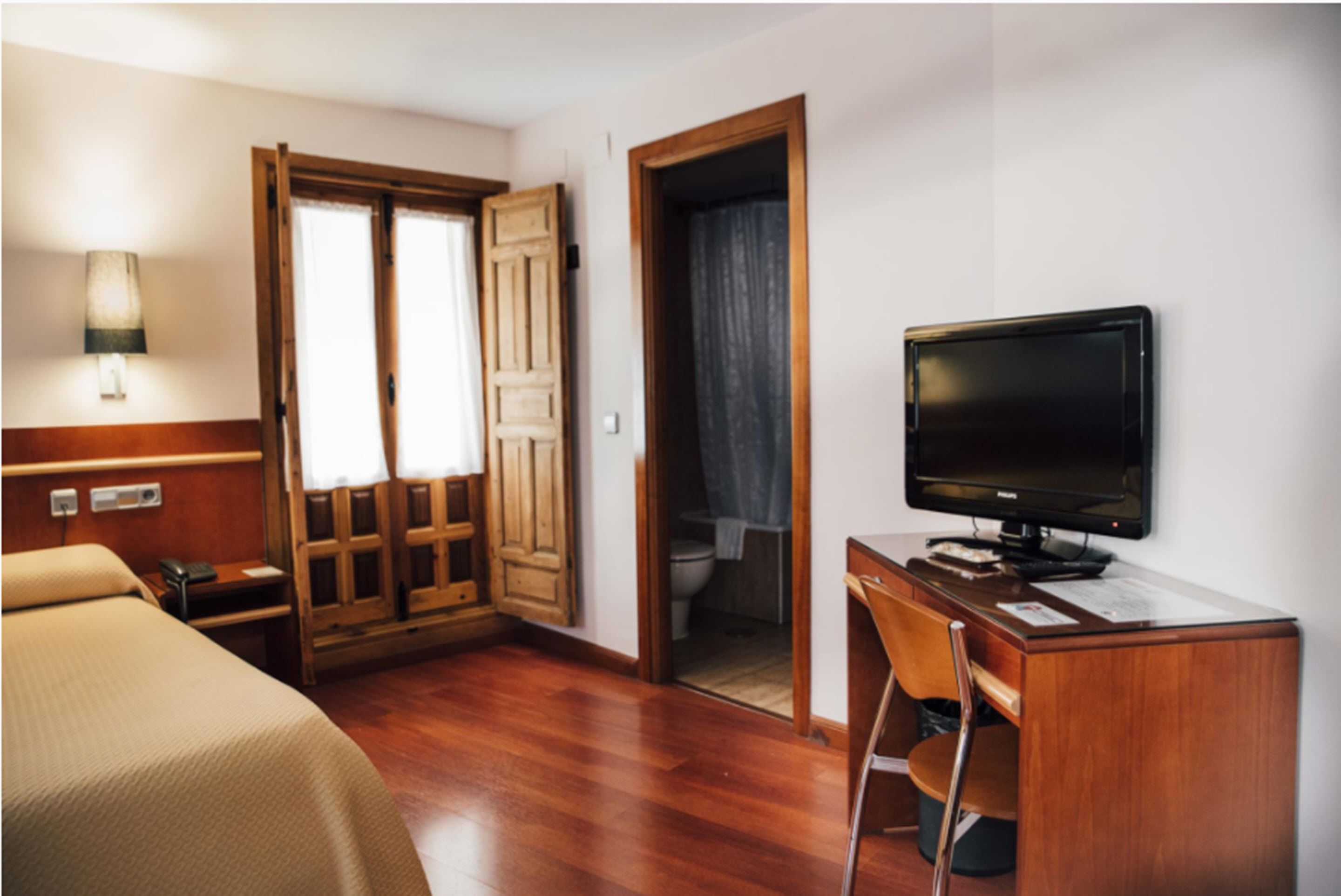 Ein Hotelzimmer mit Bett, Schreibtisch, Stuhl, Fernseher und einem durch eine offene Tür einsehbaren Badezimmer.