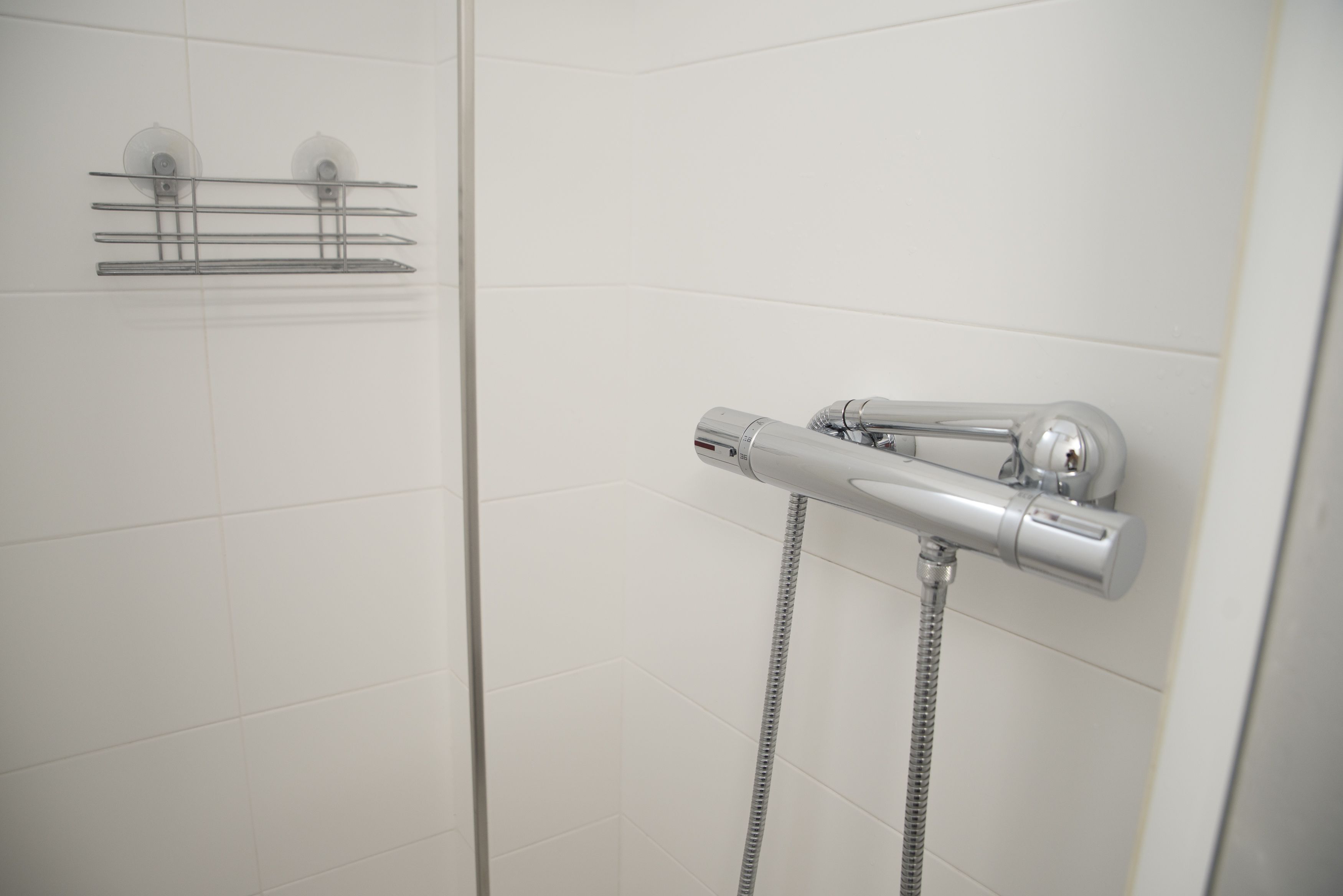 A shower with a handheld showerhead and a wall-mounted faucet.