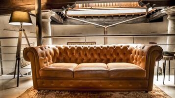 A tufted leather sofa in a lobby with a lamp, columns, and a staircase.