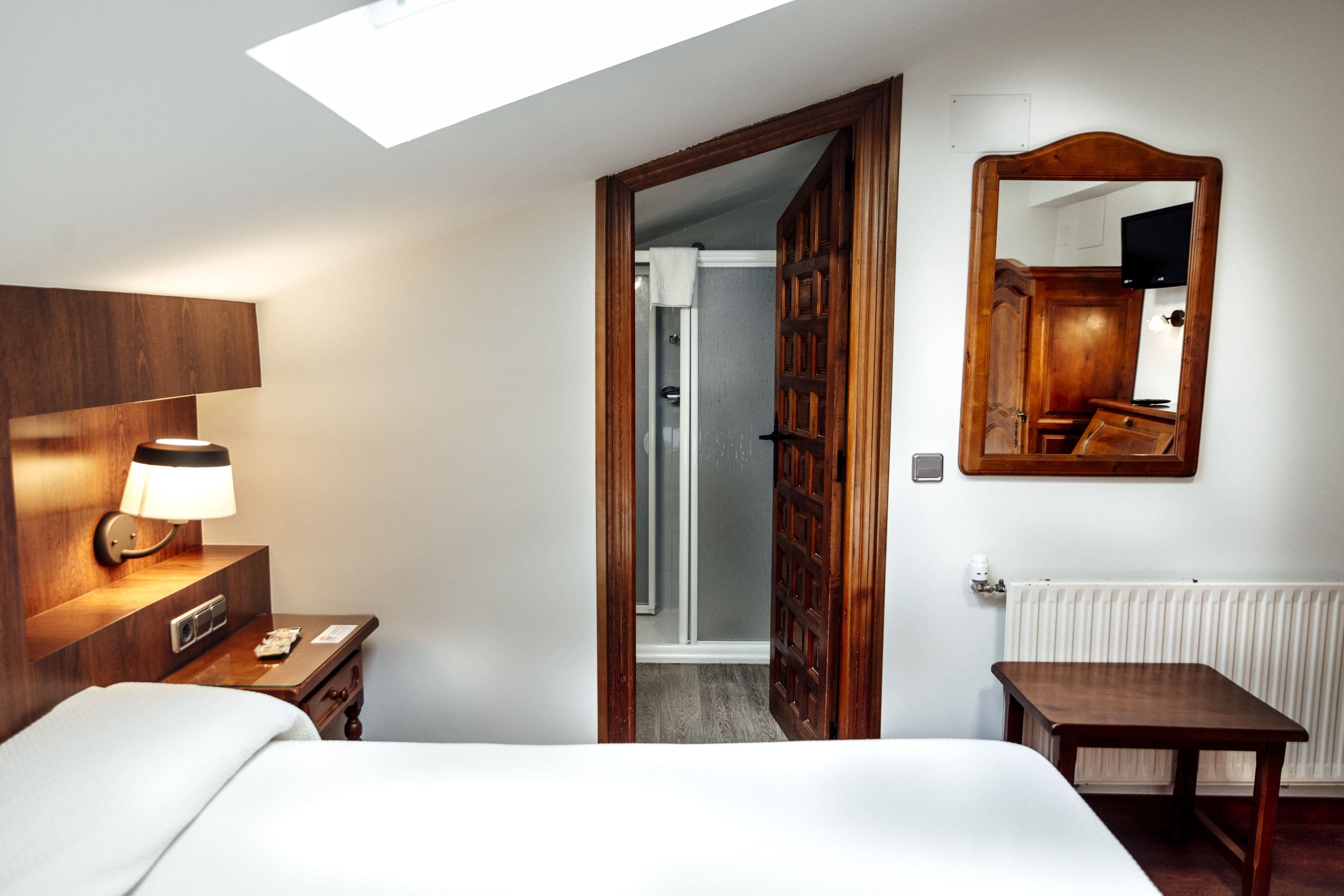Una camera d'hotel con un letto, un comodino, una lampada e un grande specchio a parete.