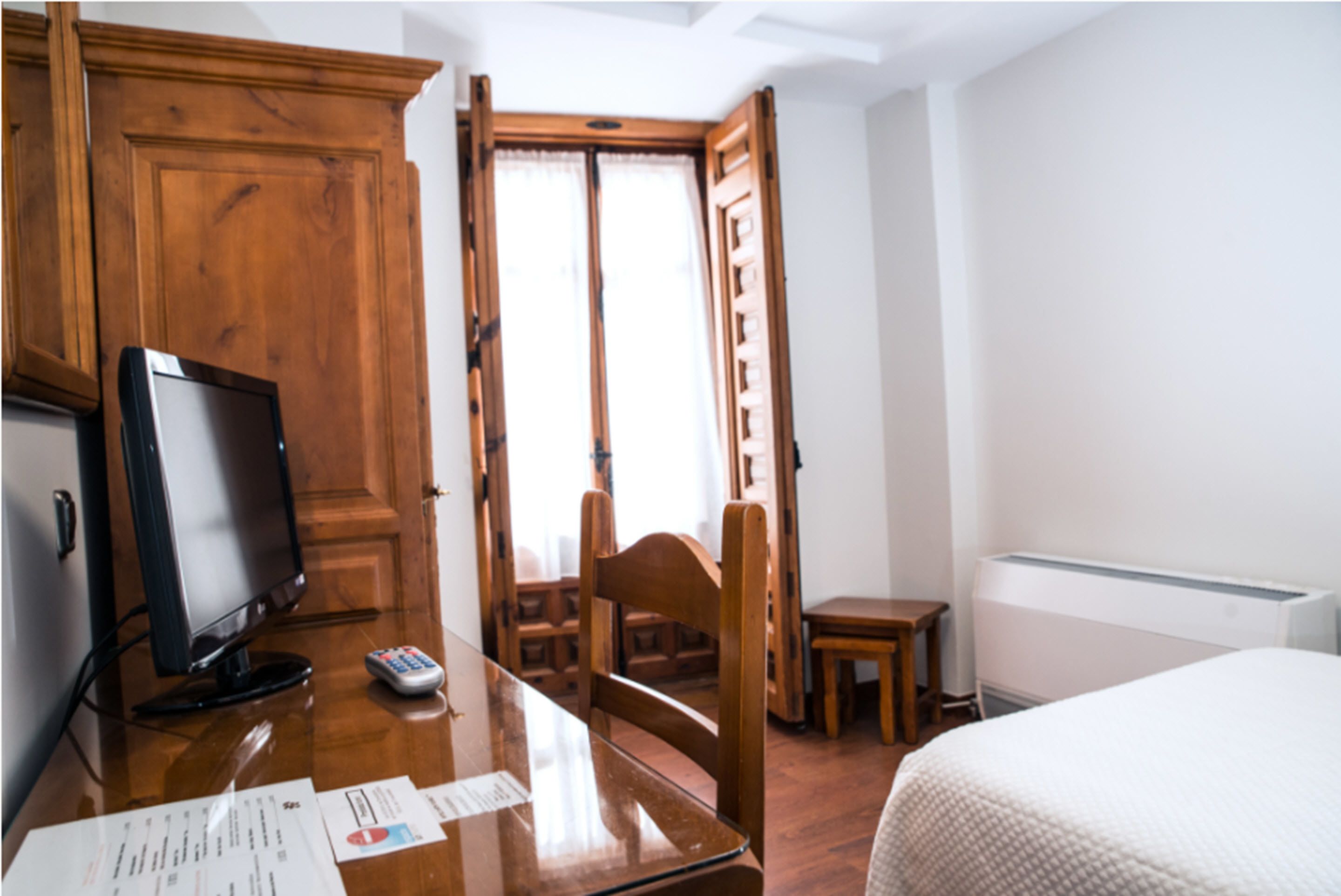 Habitación de hotel con un escritorio de madera, televisor, una silla, cama y ventana con cortinas.