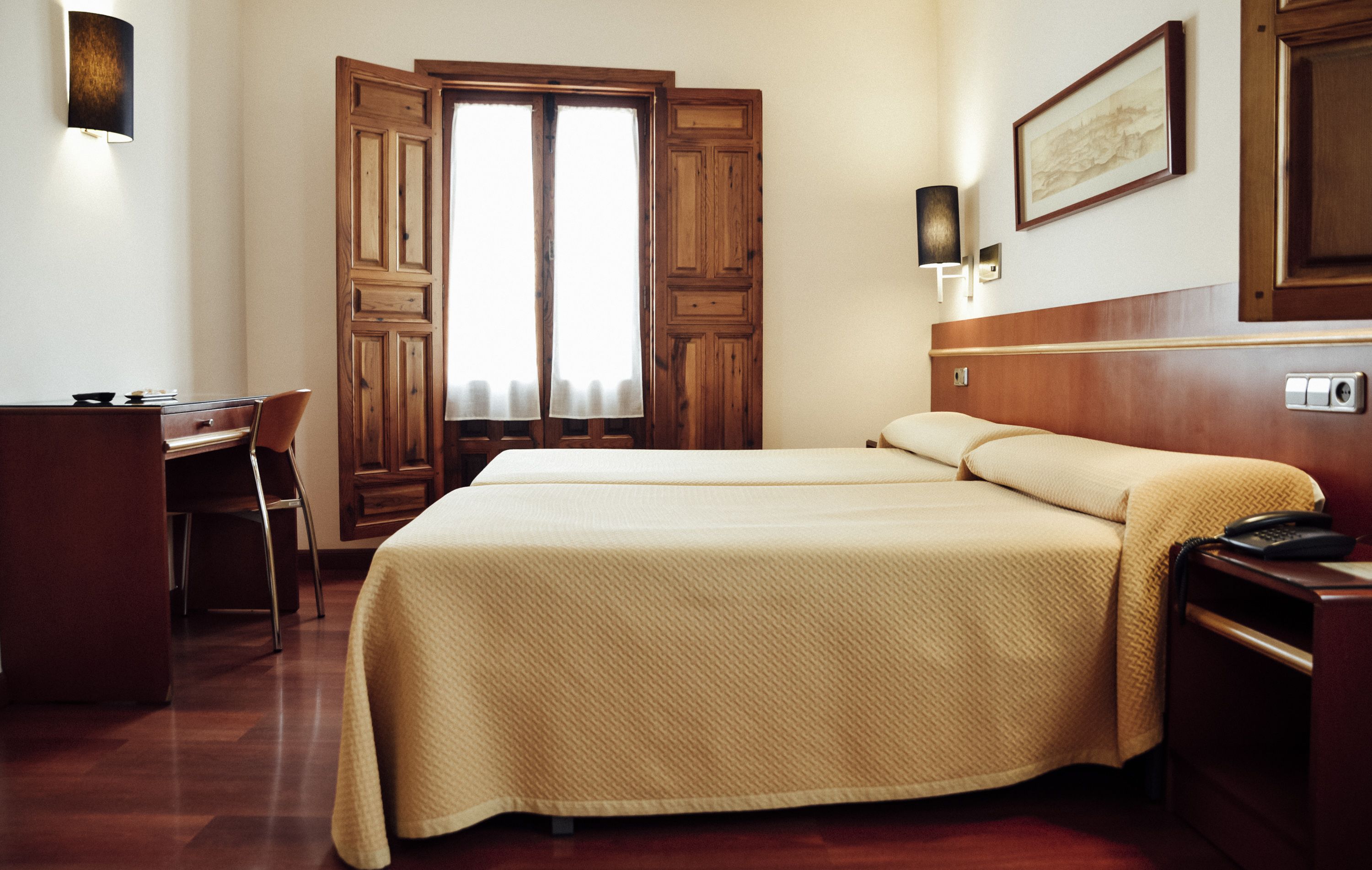 Habitación de hotel con cama, escritorio, silla y armario de madera.