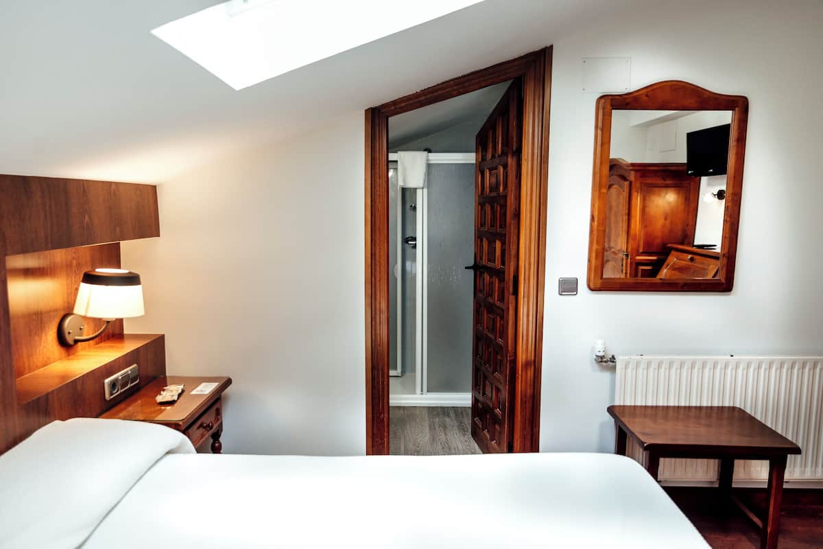 A hotel room with a bed, bedside table, lamp, and a large mirror on the wall.