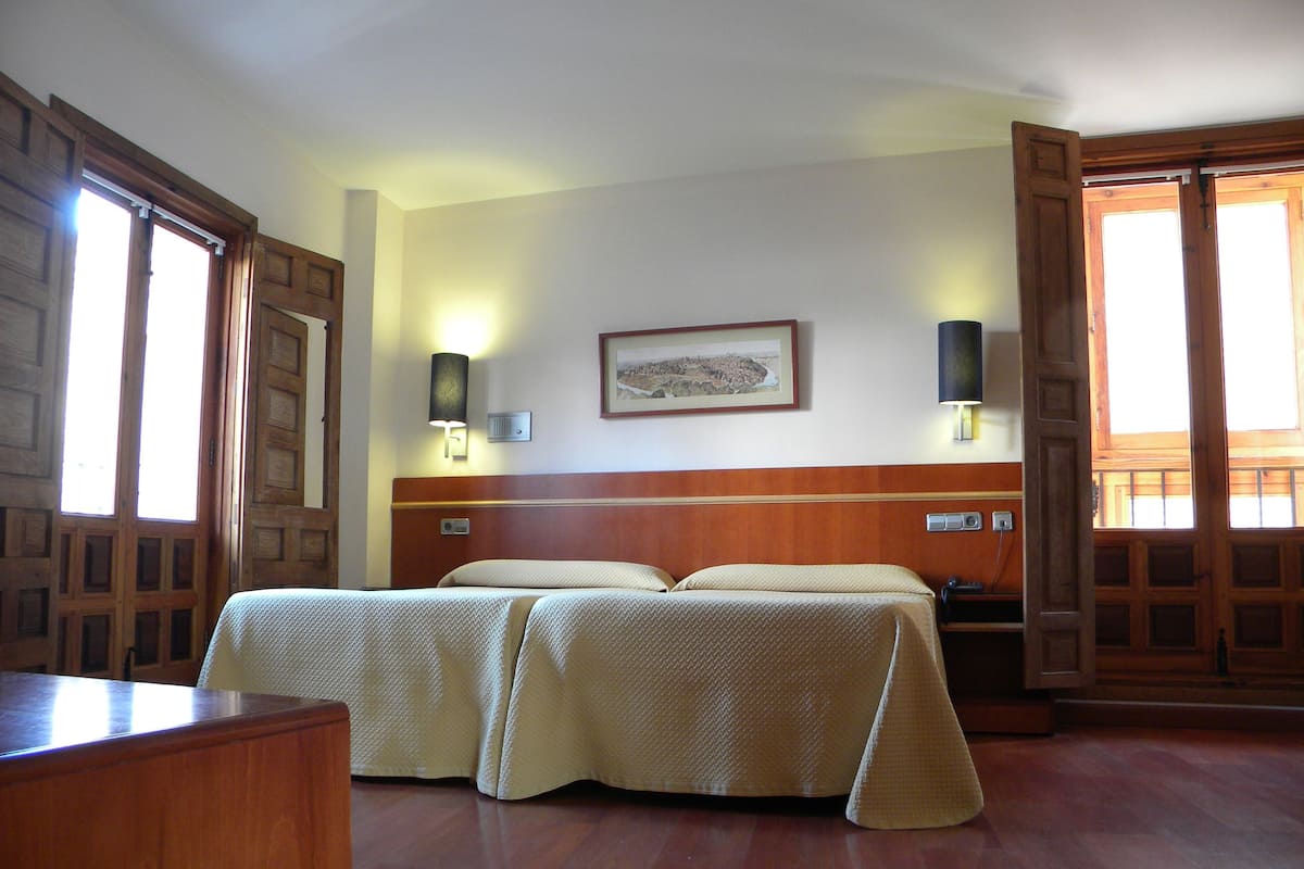 A hotel room with two beds, wooden headboard, wall-mounted lamps, and a framed picture on the wall.