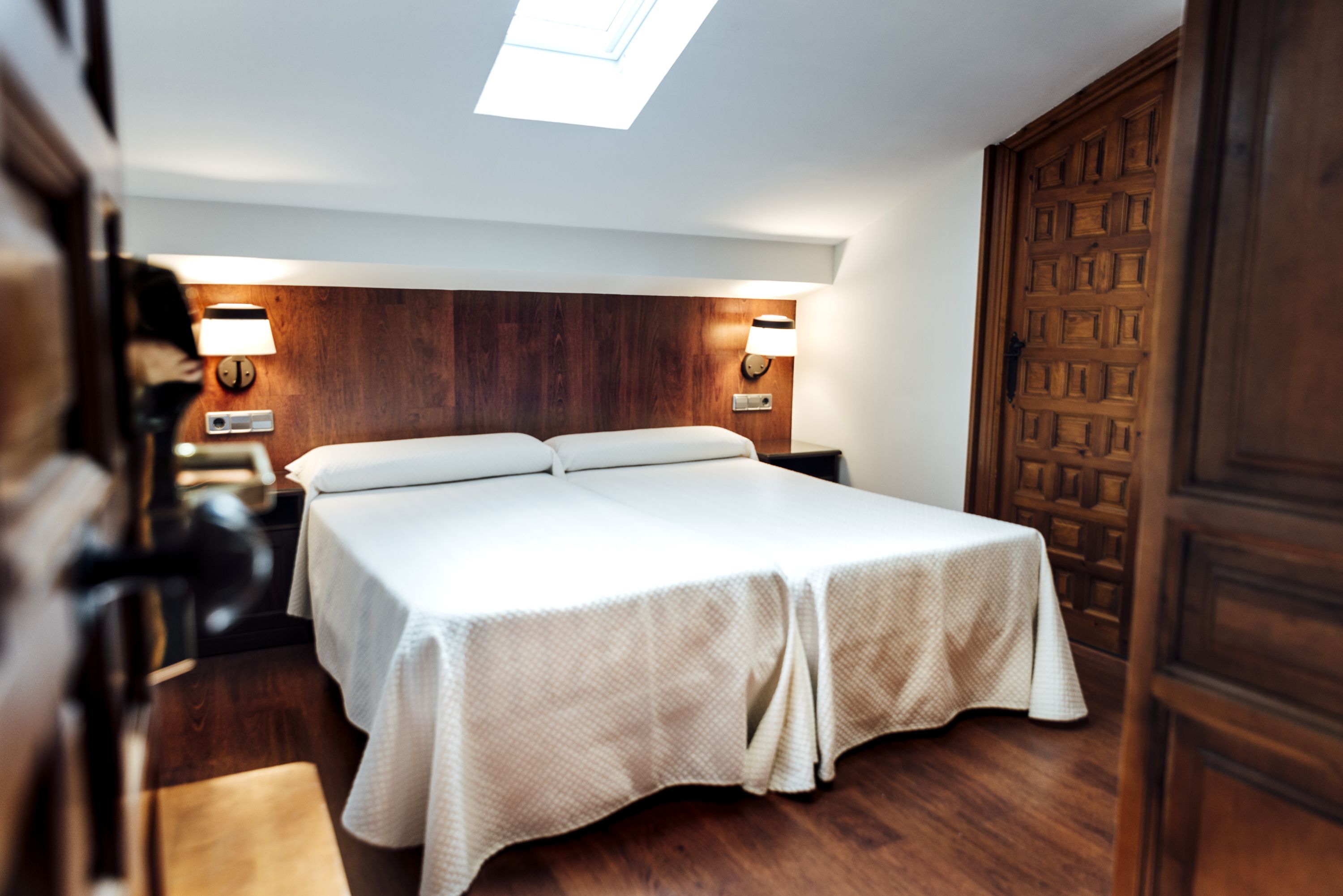 A hotel room with a bed, wooden headboard, two bedside lamps, and a wooden door.