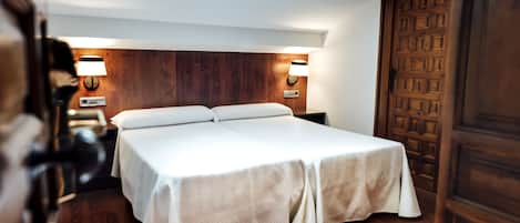A hotel room with a bed, wooden headboard, two bedside lamps, and a wooden door.