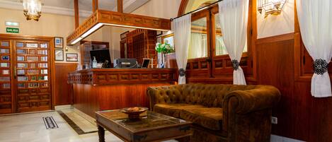 Un vestíbulo con un mostrador de recepción de madera, un sofá marrón y una mesa de centro de cristal.