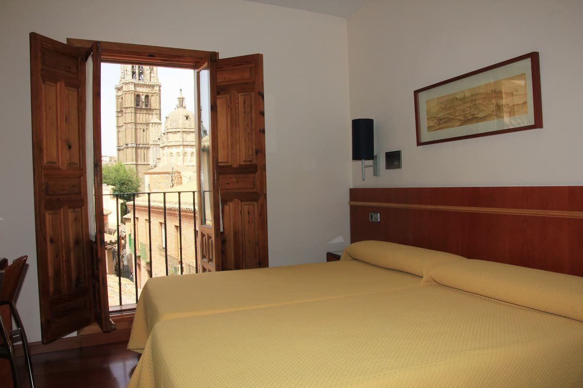 A hotel room with a bed, wooden door, and a view of a cathedral through the open door.