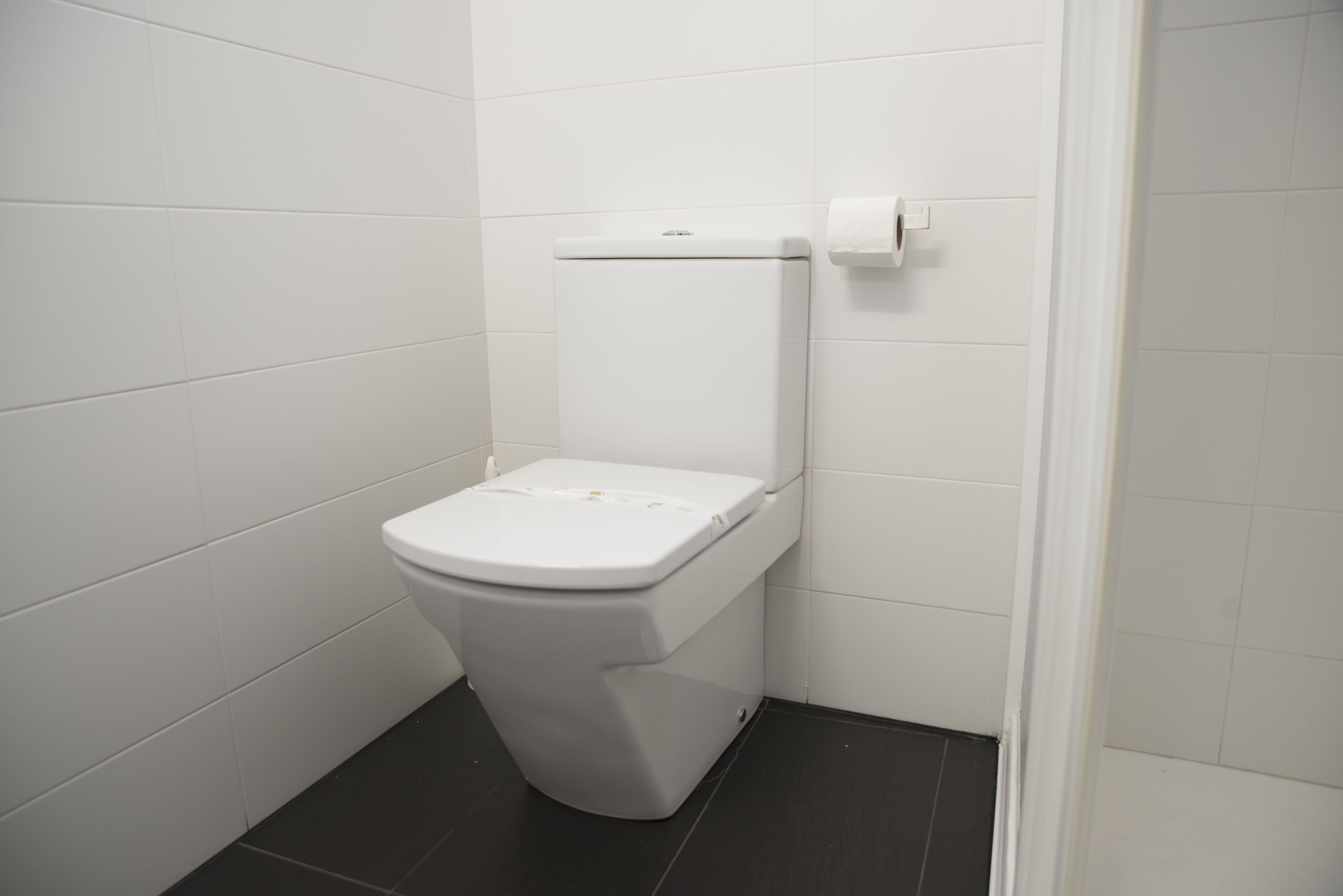 Inodoro blanco estándar con dispensador de toallas de papel en un baño pequeño con azulejos.