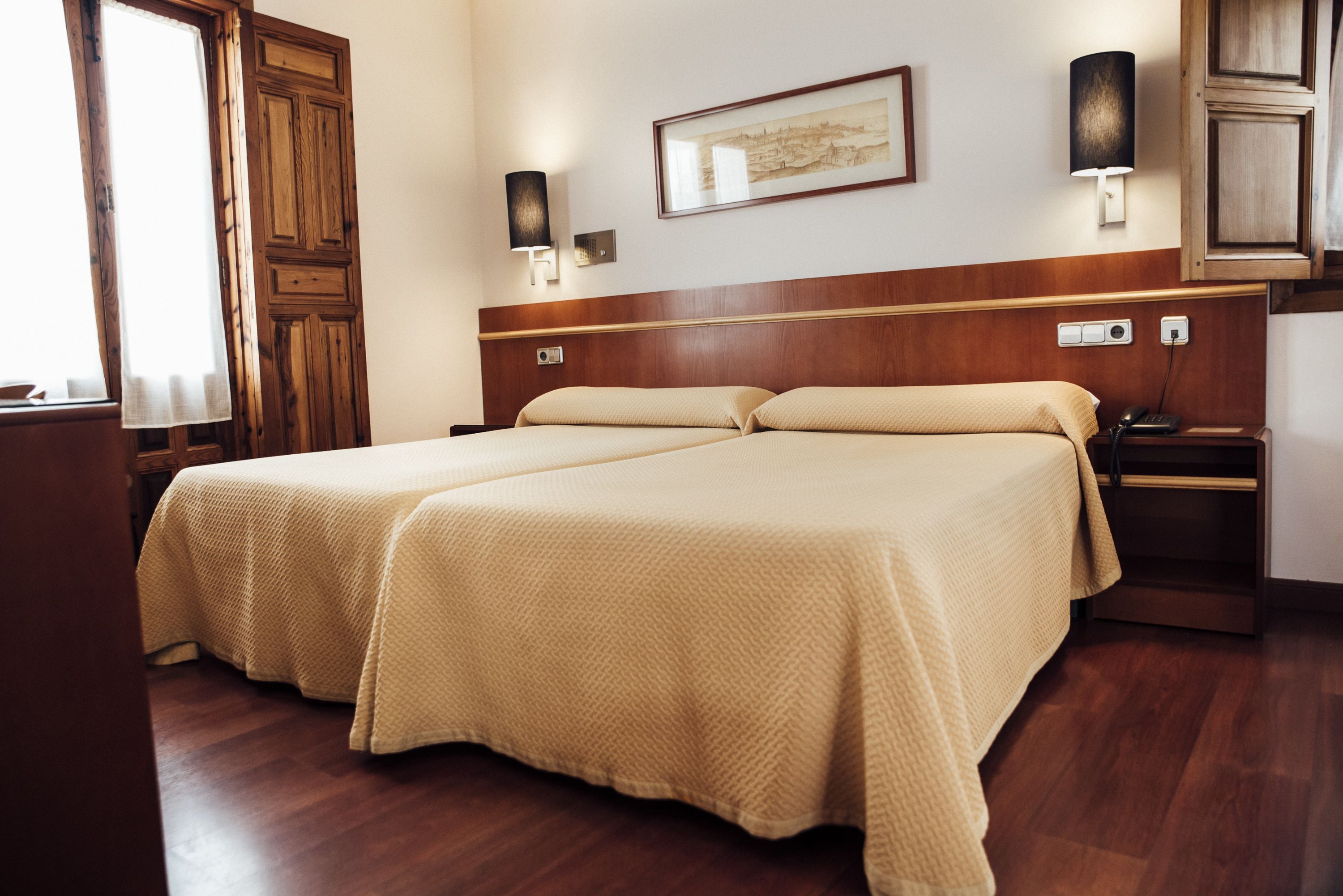 A double bed with a beige bedspread in a hotel room.