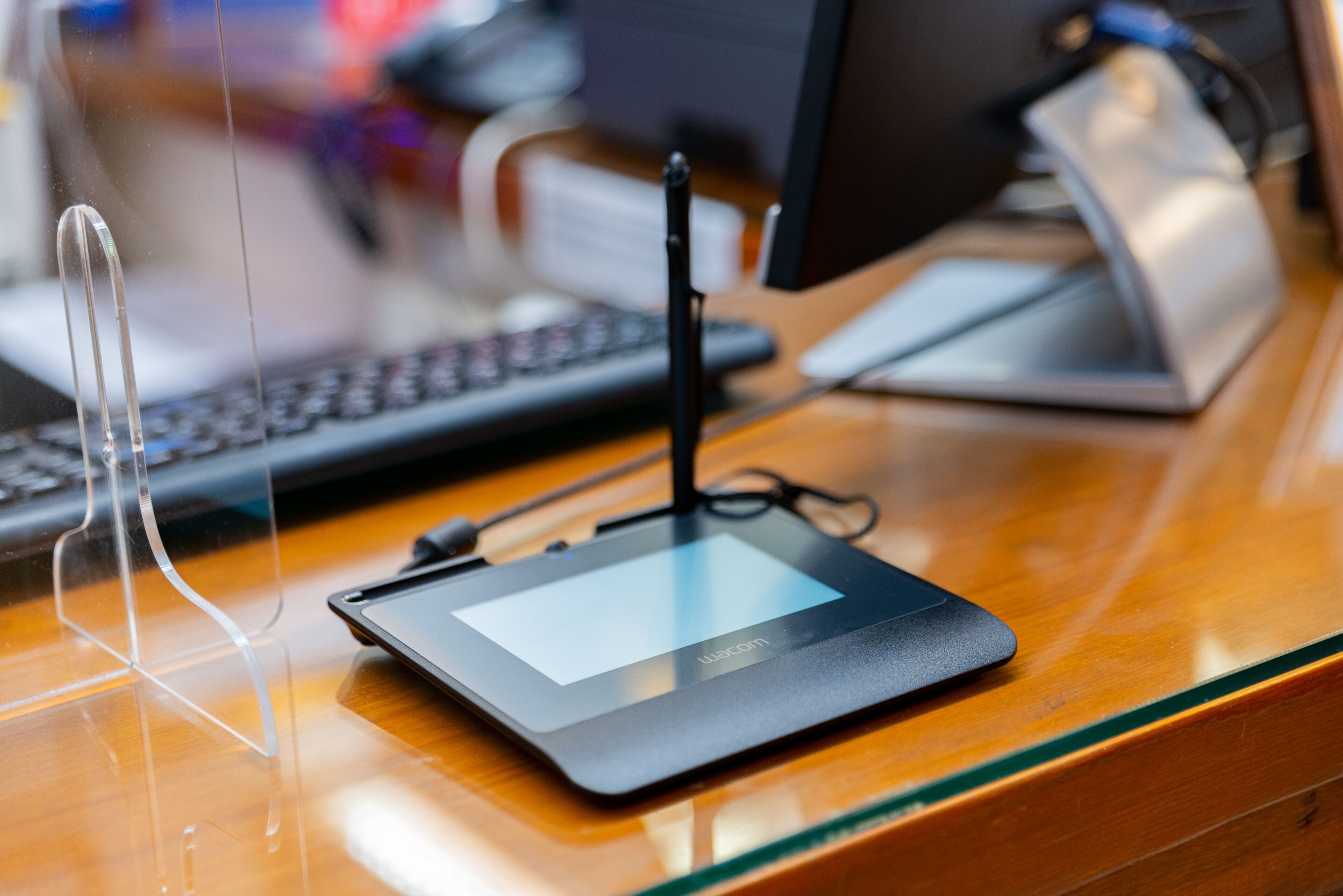 A tablet on a wooden desk with a keyboard and a monitor in the background.
