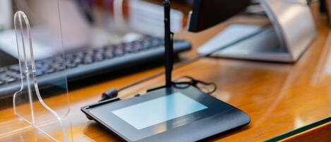 A tablet on a wooden desk with a keyboard and a monitor in the background.