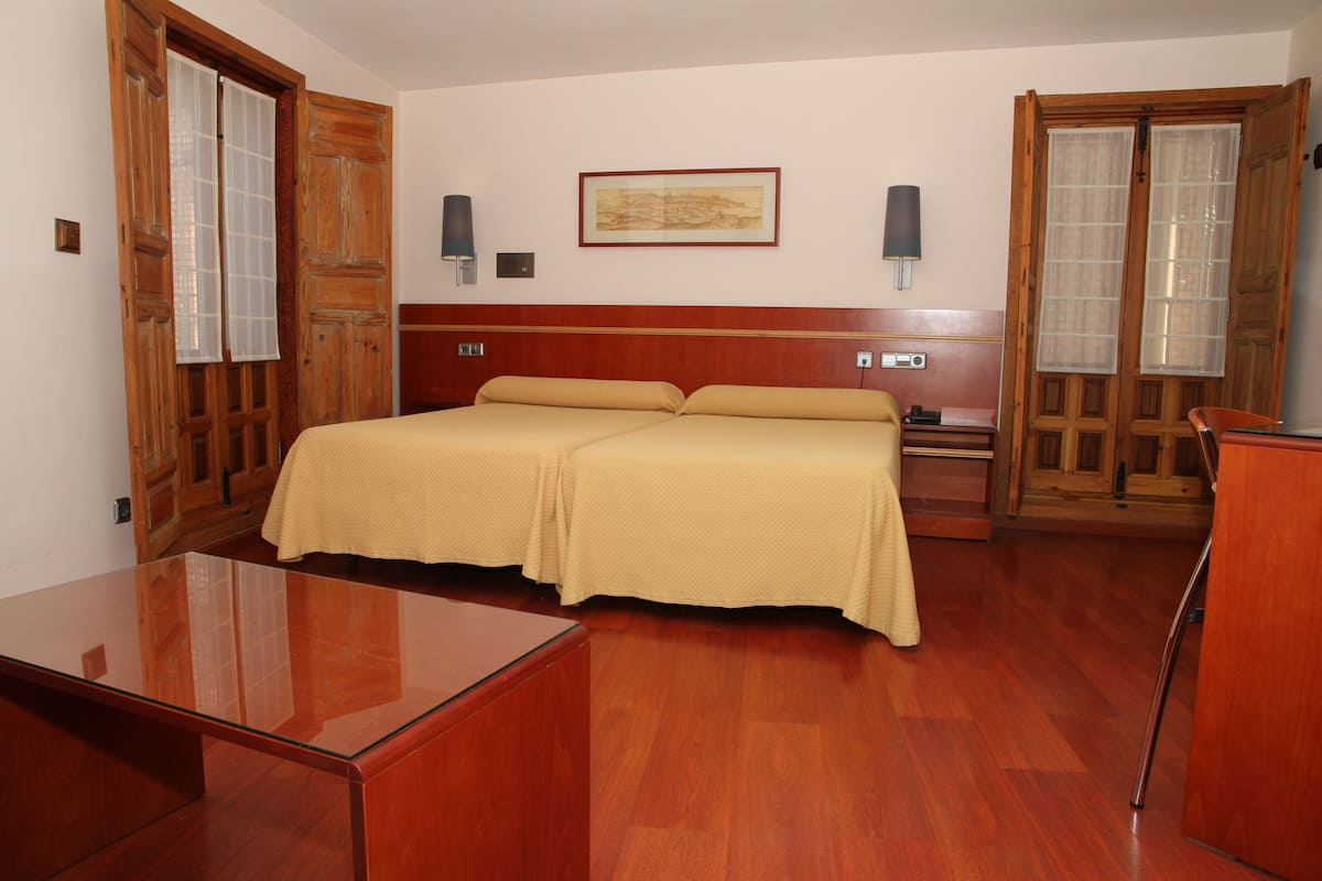 A hotel room with a wooden bed, a bedside table, a desk, and a chair.