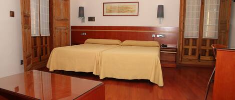Una habitación de hotel con una cama de madera, una mesita de noche, un escritorio y una silla.