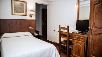 Ein Hotelzimmer mit einem Bett, einem Schreibtisch mit Computer, einem Holzschrank, einem an der Wand befestigten Fernseher und einem gerahmten Bild.