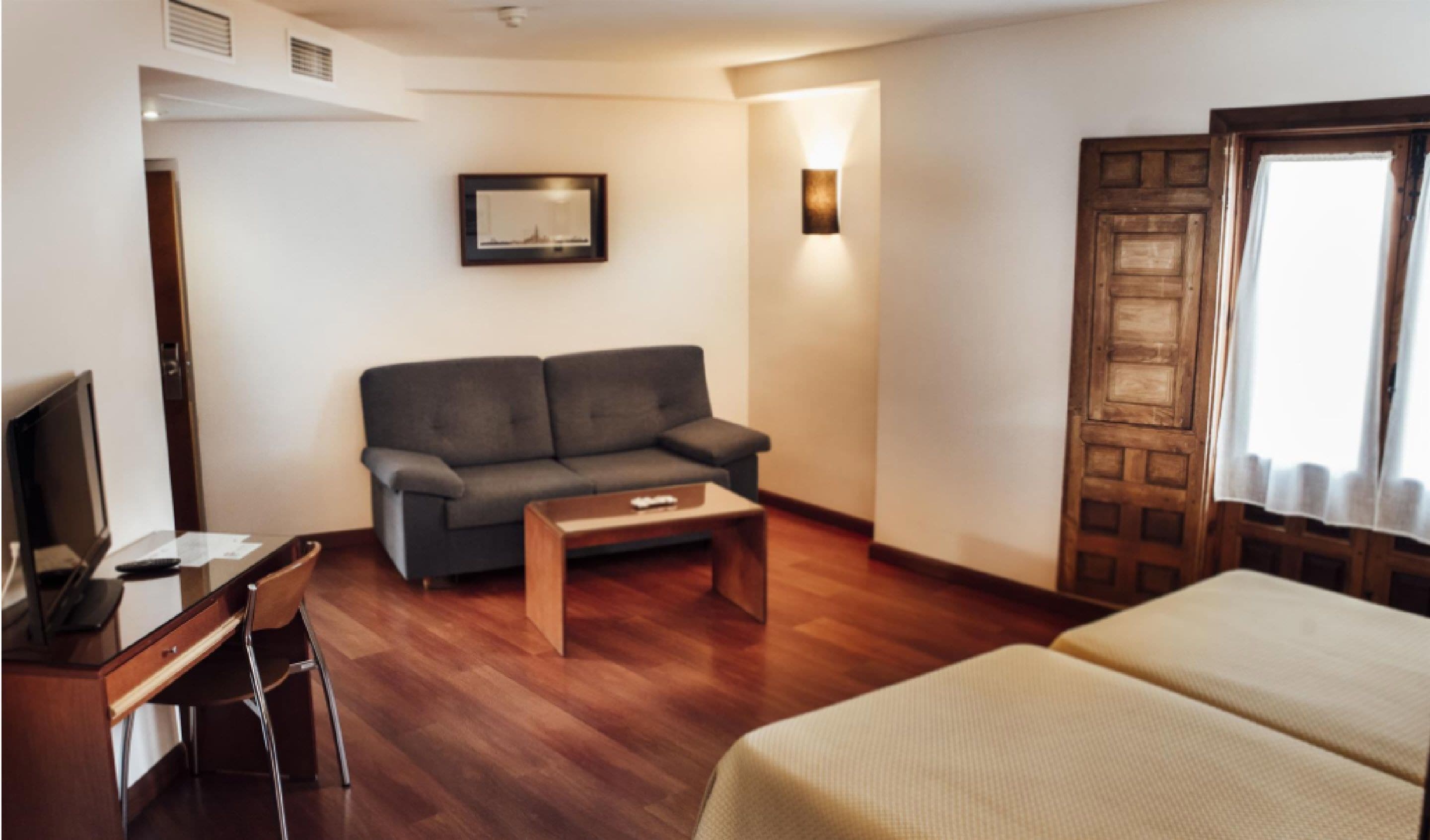 A hotel room with a sofa, a desk with a chair, a bed, and a wooden door.
