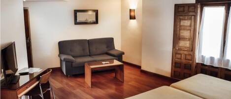 A hotel room with a sofa, a desk with a chair, a bed, and a wooden door.