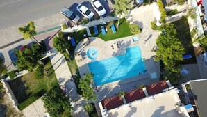 Eine Luftaufnahme eines Anwesens mit Schwimmbad, Liegestühlen und einem Parkplatz mit mehreren Autos.