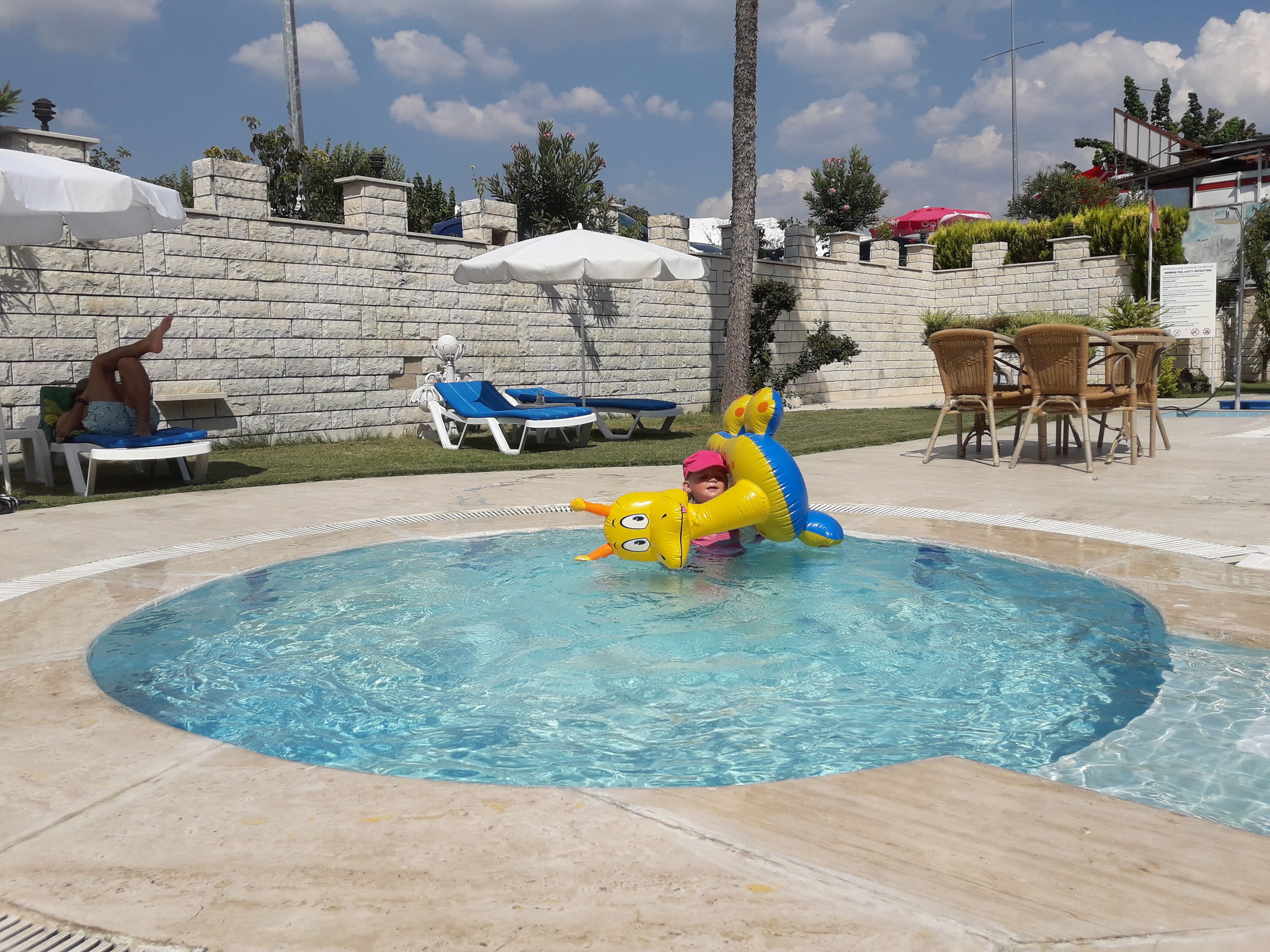 A swimming pool with lounge chairs and a stone wall in the background.