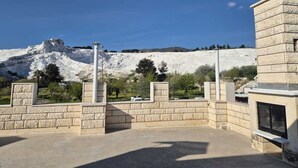 Ein Innenhof mit Steinmauern, einer Pergola und Blick auf einen weißen Berg.