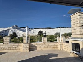 A courtyard with stone walls, a pergola, and a view of a white mountain.