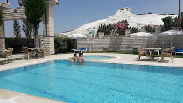 Relax by the serene pool surrounded by comfortable seating and a scenic stone bridge.