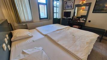 A hotel room with two beds, a desk, a chair, a TV, and a window with curtains.