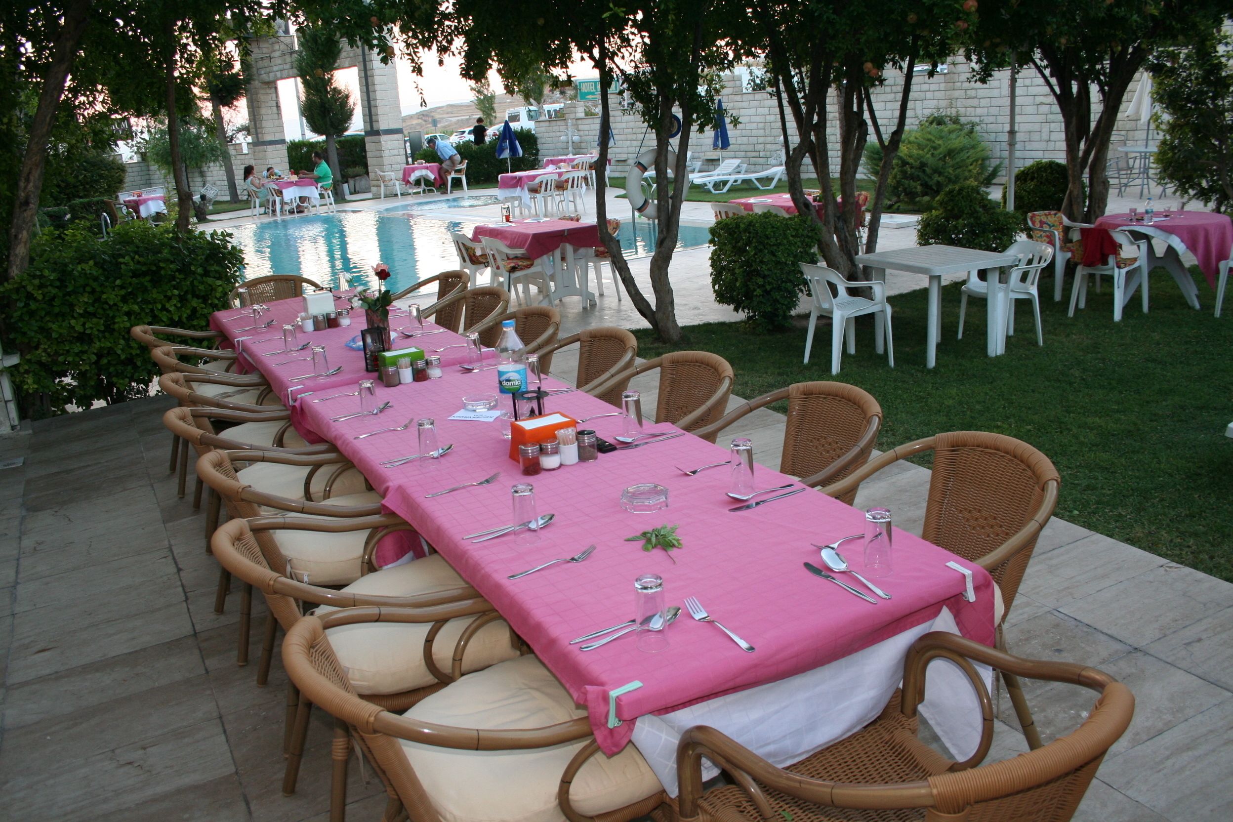 An outdoor dining area with a long table set for a meal, surrounded by wicker chairs.