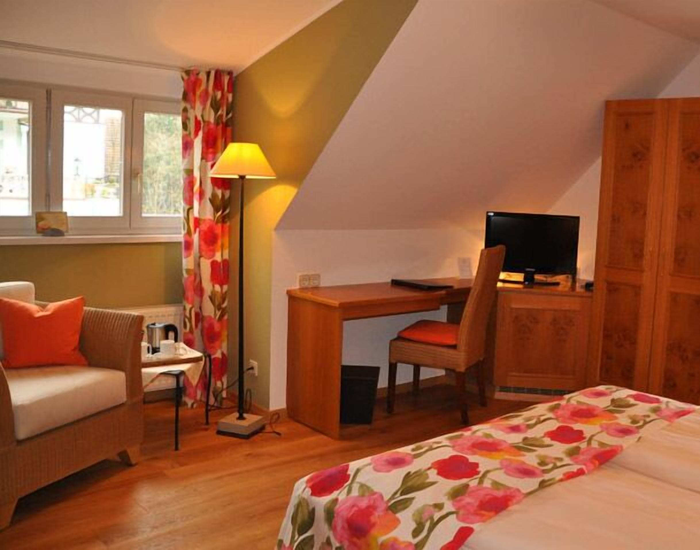 A cozy bedroom with a bed, a desk, a chair, a television, and a window with curtains.