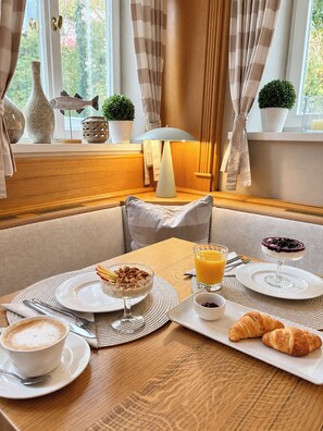 A breakfast setting with a table set for two, including plates with food, a glass of orange juice, a croissant, and a cup of coffee. - Hotel Fischerhaus (Starnberg)