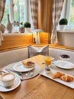 Un desayuno preparado para dos personas, con platos de comida, un vaso de jugo de naranja, un croissant y una taza de café.