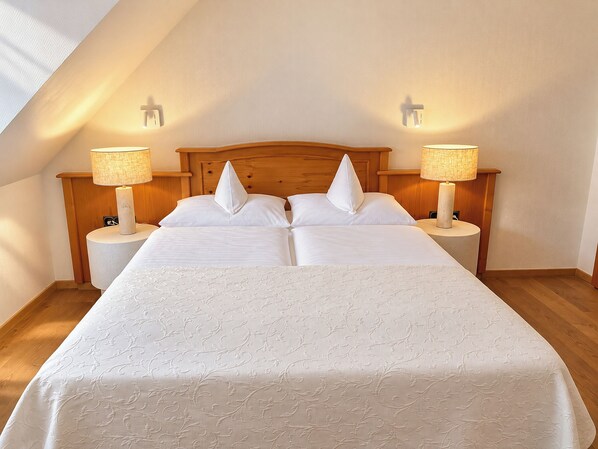 A double bed with a wooden headboard, two bedside lamps, and a textured white bedspread.