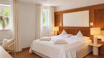 A hotel room with a large bed, two bedside tables with lamps, a window with curtains, and a chair.