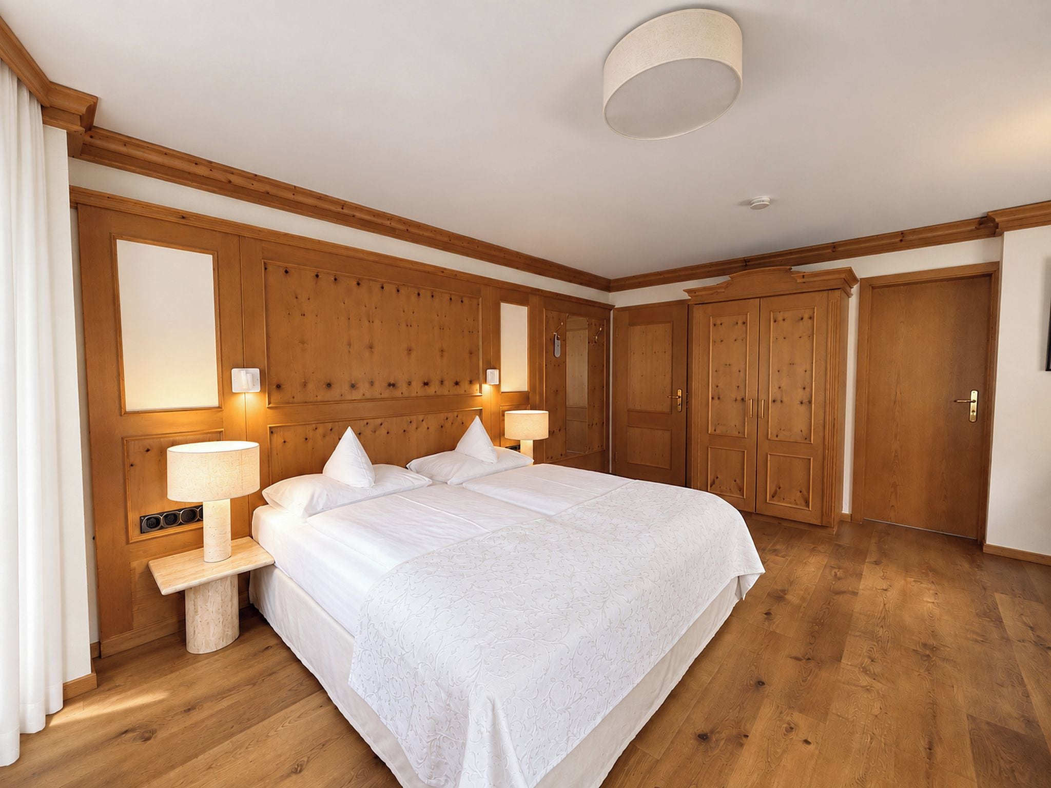 A hotel room with a large bed, two bedside lamps, a wooden headboard, and a wardrobe.